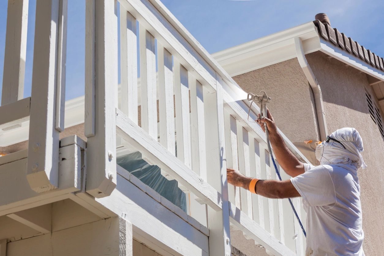 A painter spraying a white porch railing